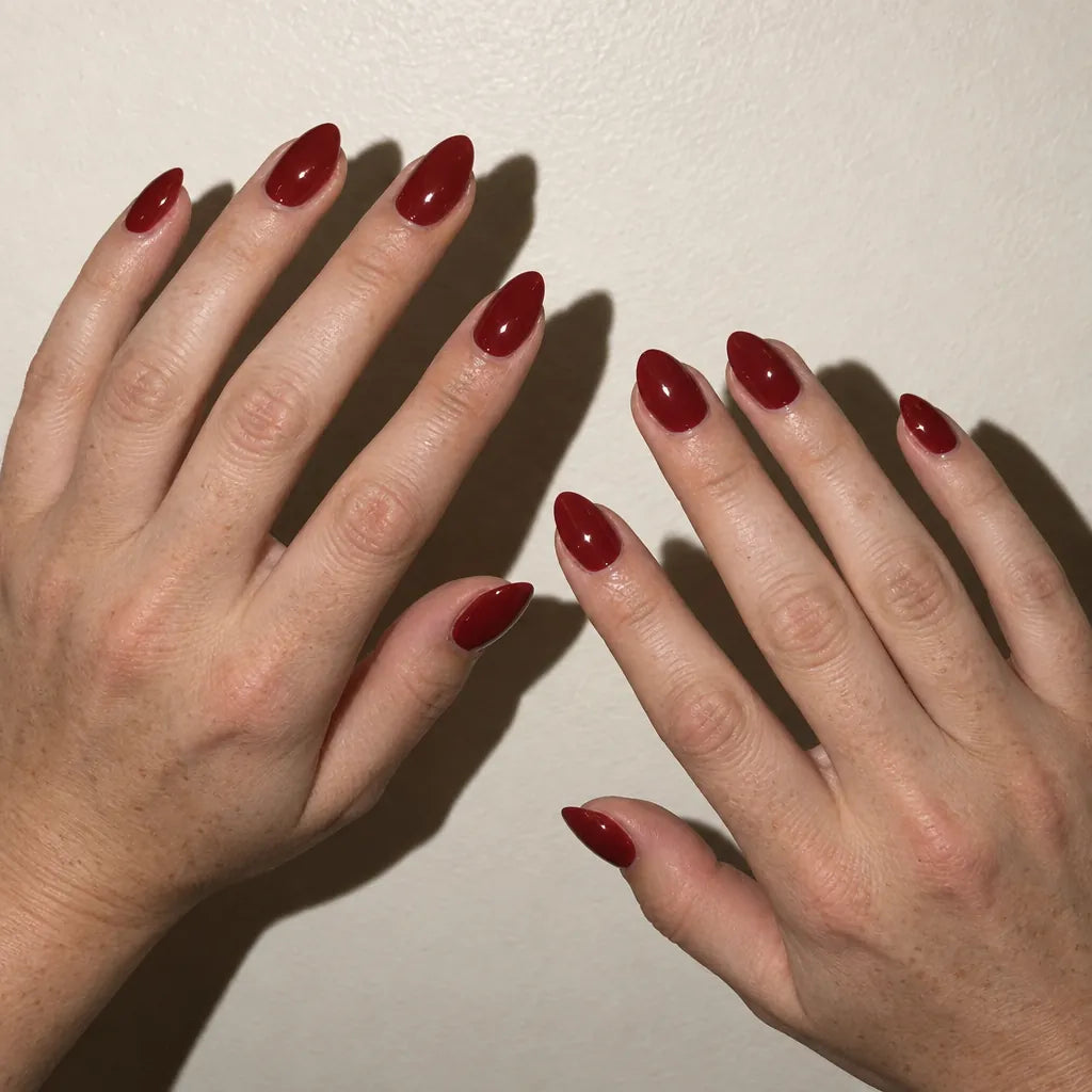 Almond nails in a deep cherry red against a knit throw