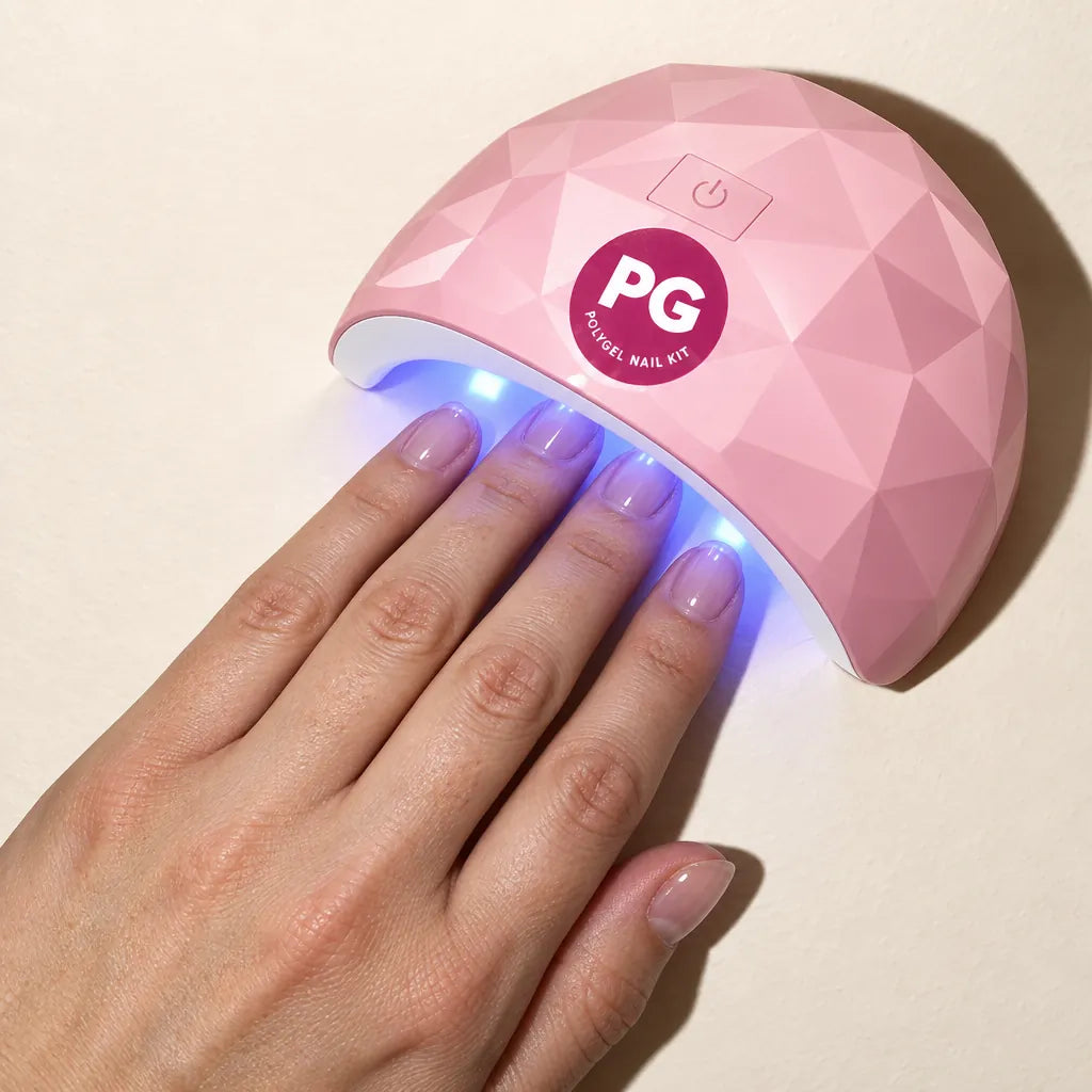 A hand resting under the pink LED lamp while the gel cures
